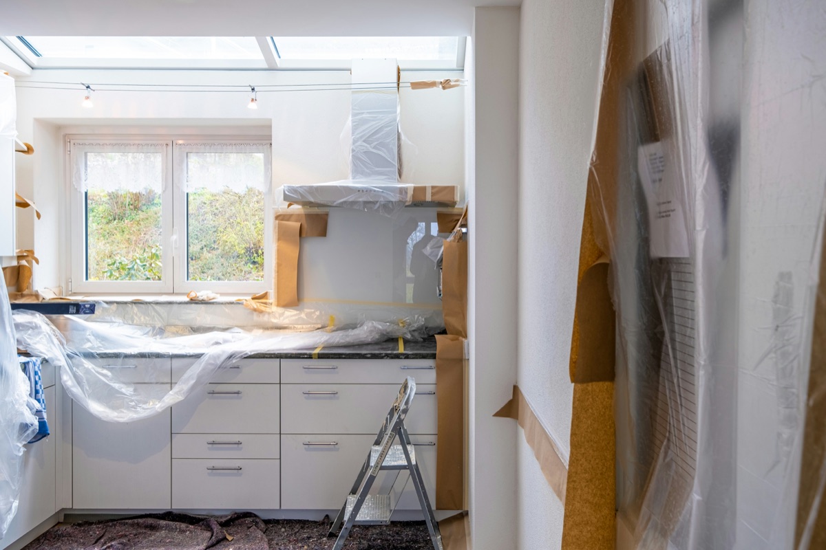 Kitchen mid-renovation with cabinets masked off and range hood being fitted