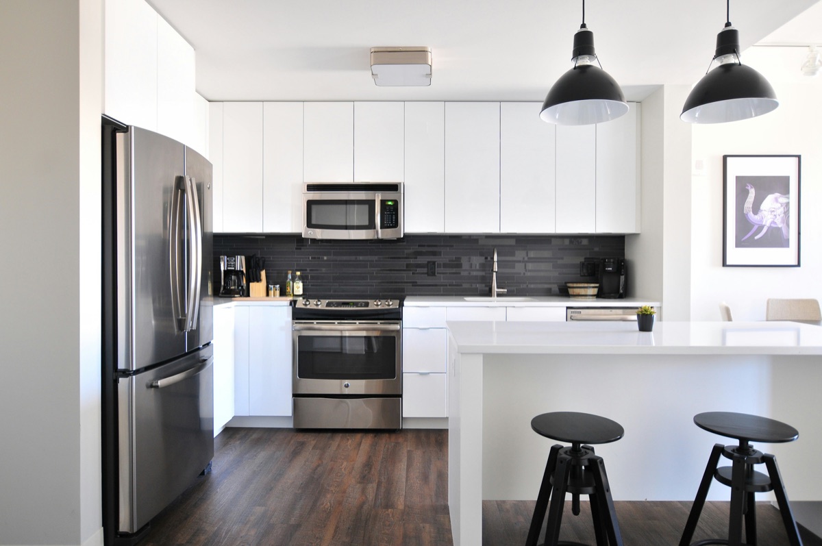 Modern white kitchen with island, dark backsplash and stainless appliances